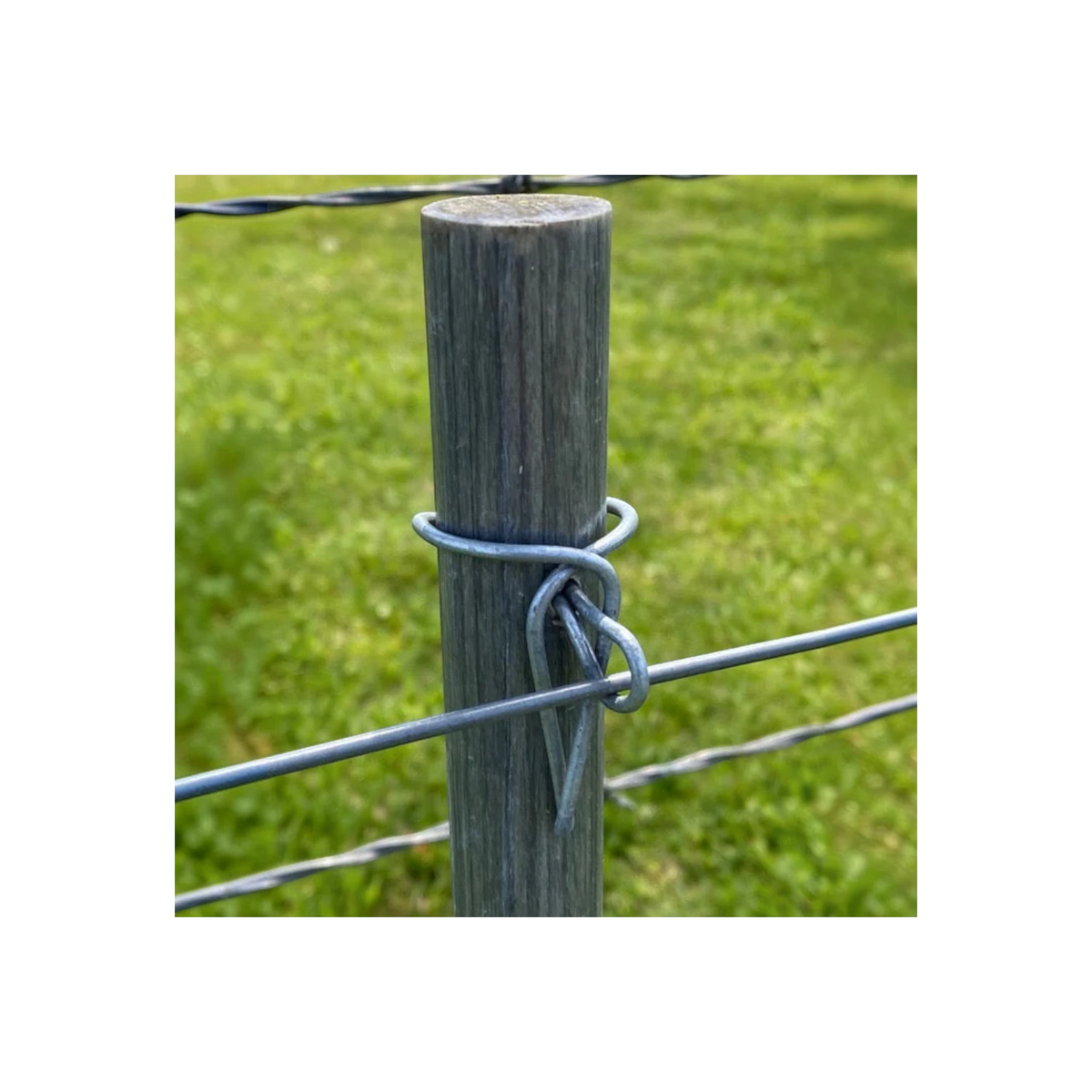USA Grazing Systems 14-gauge metal cotter pin securing a wire to a wooden fence post in a grassy field