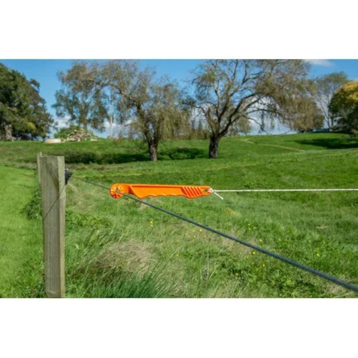 USA Grazing Systems Gallagher non-conductive orange plastic gate handle attached to an electric fence in a green pasture.