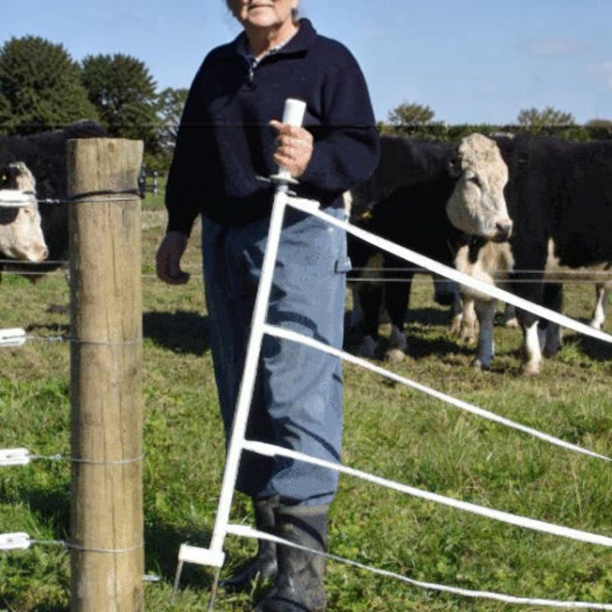 USA Grazing Systems Taragate multi-strand electric fence gate held by a farmer in a pasture with cattle in the background